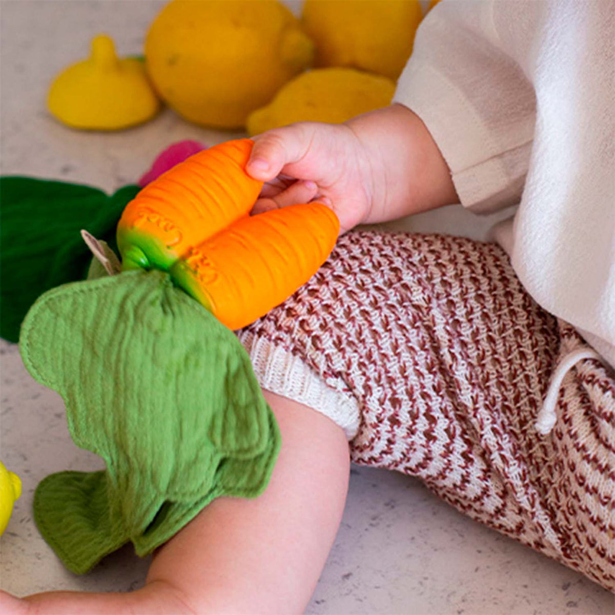 Oli&Carol mini doudou-bijtring Cathy the Carrot met mousseline blad in kinderhand