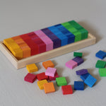Honderd vierkante houten mozaïekstenen van Bauspiel in tien kleuren en een houten frame. 