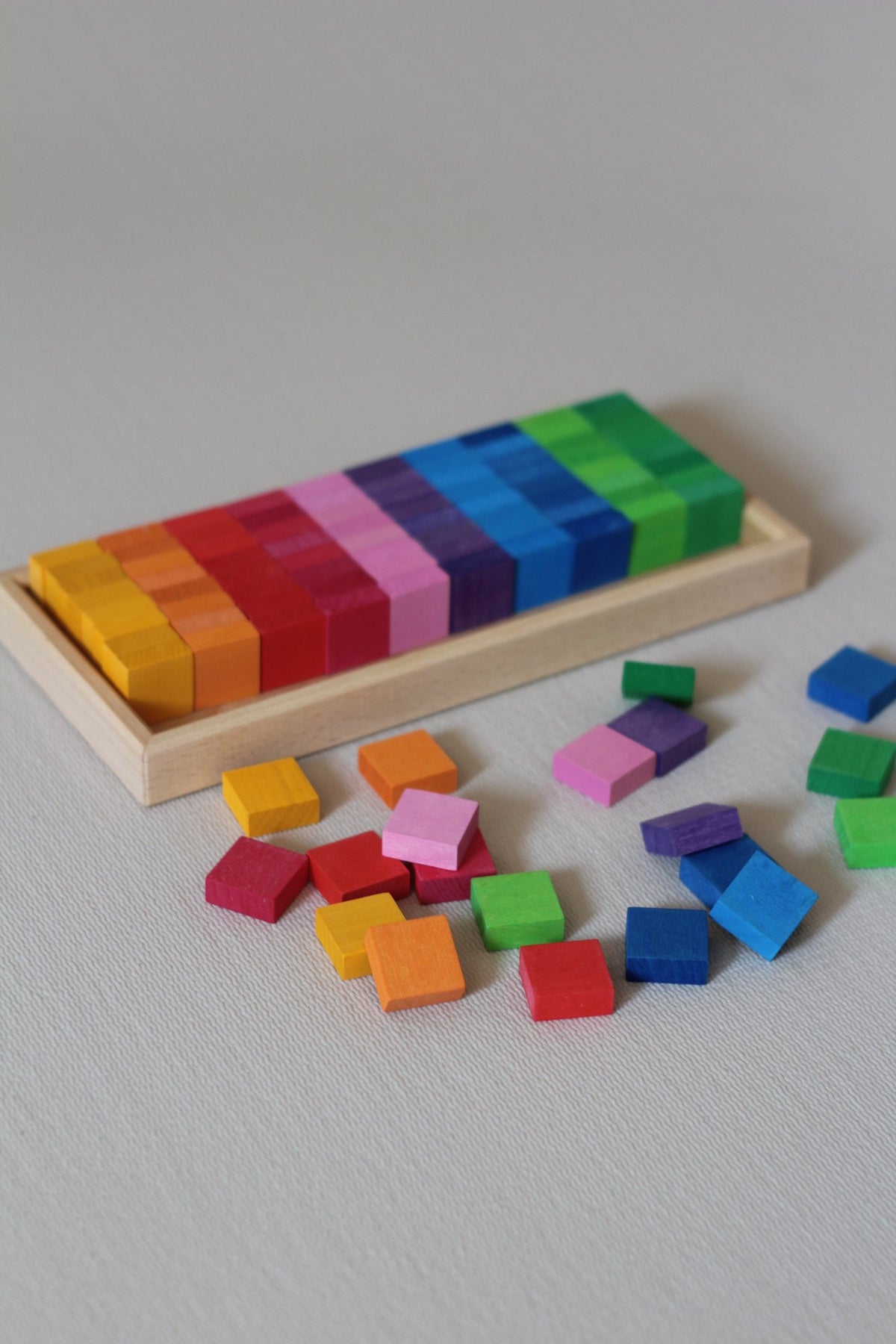 Honderd vierkante houten mozaïekstenen van Bauspiel in tien kleuren en een houten frame. 