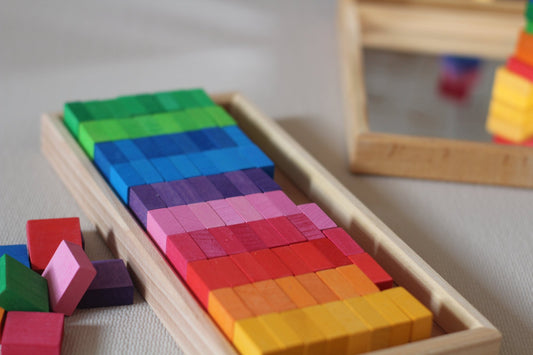 Honderd vierkante houten mozaïekstenen van Bauspiel in tien kleuren en een houten frame op de grond